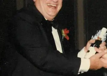 George J. Lavin, Jr. smiling in a tuxedo at a formal event, holding an award or celebratory item