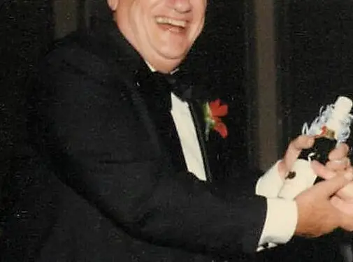 George J. Lavin, Jr. smiling in a tuxedo at a formal event, holding an award or celebratory item